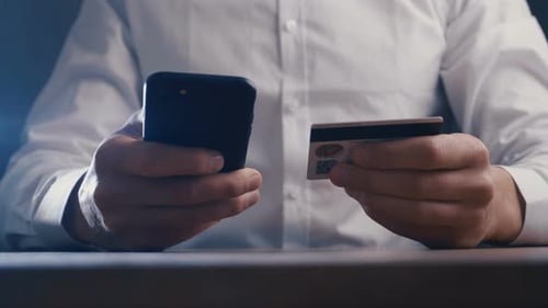 Businessman in White Shirt Using Smartphone for Online Shopping with Credit Card at Workplace