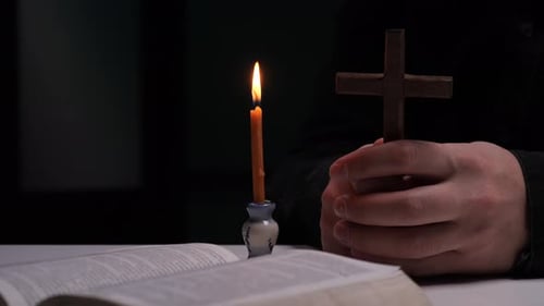 Priest Praying with Wooden Cross and Burning Candle in Church