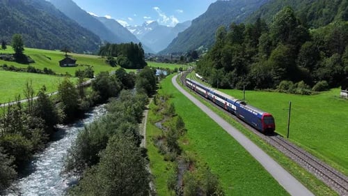 Un train pittoresque traverse une vallée suisse luxuriante au bord de la rivière et des montagnes par une journée ensoleillée