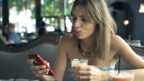 Young, Happy Woman Drinking Coffee and Texting on Smartphone in Cafe 30s