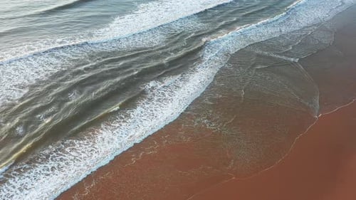 Drone Shot of Waves Rolling Onto Wet Sandy Shore with White Foam