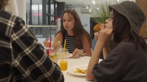 A woman with her kids is having lunch at a table in a mall food court.