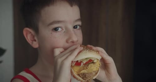 Young Boy Eating a Large Burger Indoors
