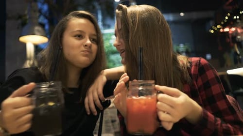 Happy teenage girlfriends enjoying fresh drinks and casual conversation in cafe