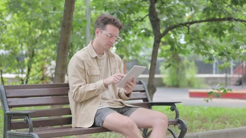 Young Adult Using Tablet on Bench in Park