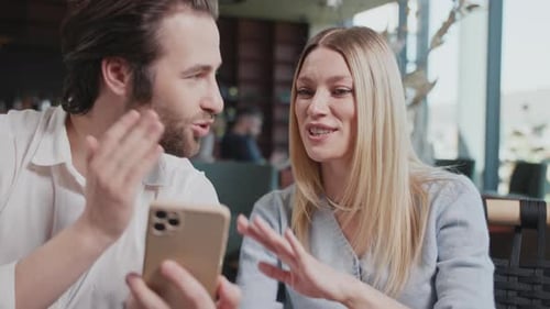 Cute Happy Couple with a Smartphone in a Cafe Talking Discussing Smiling Sitting Modern Interior
