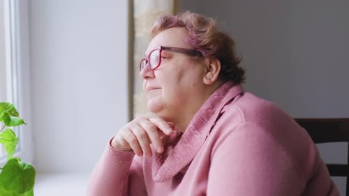Senior Woman Thoughtfully Looking Out Window Indoors