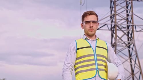 A designer inspects a high voltage tower. An engineer in a hard hat servicing a power transmission p