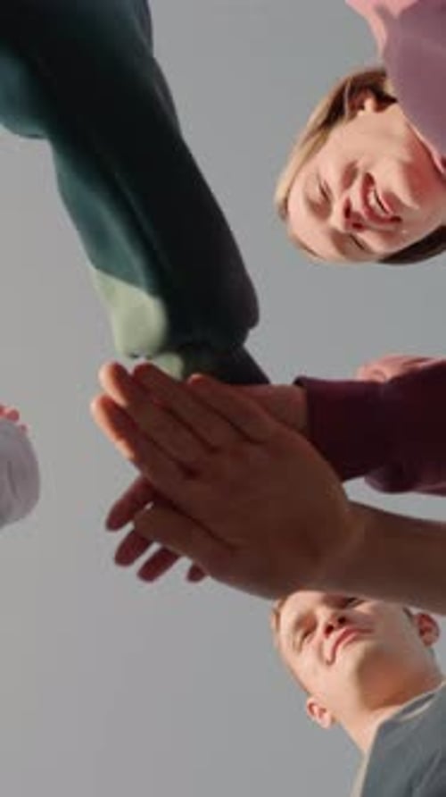 Upward View of Team Members Joining Hands with Sunlight Glow