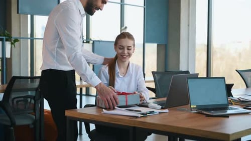 Giving present for a woman. Two employees are working in the office.