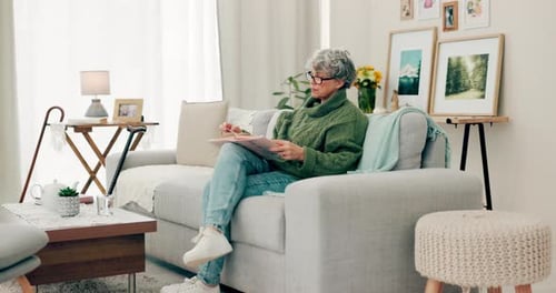 Senior woman, book and reading to relax in living room for story, novel and knowledge