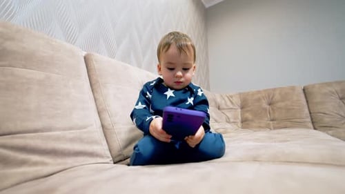 Adorable Child Plays with Mobile Phone on Couch