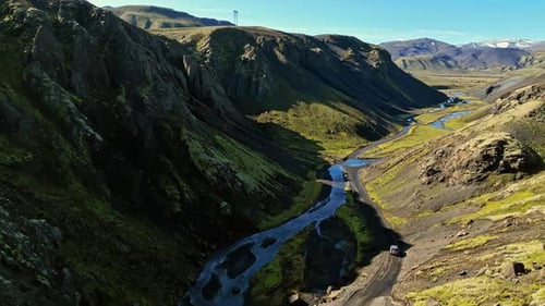 Aerial view of off-road vehicles navigating a narrow river valley between towering cliffs,
