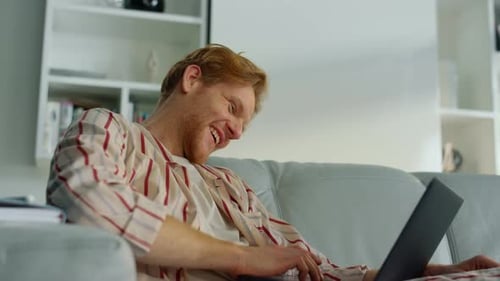 Smiling Man Relaxing on Couch Using Laptop