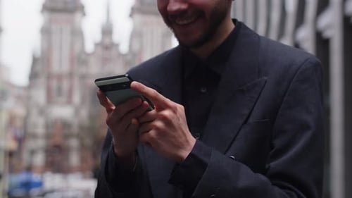 Cropped View of a Bearded Man Who Stands on the Street and Taps on the Smartphone Screen A Man in a