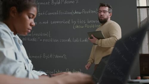 Männlicher IT-Lehrer erklärt während des Unterrichts den Codierungsalgorithmus an der Tafel