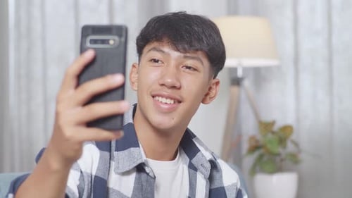 Close Up Of Asian Teen Boy Having Video Call On Smartphone While Sitting On Sofa In The Living Room