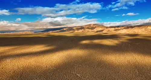 Dry deserted land with some spots of desert plants. Clouds float by the sky and throw shadows