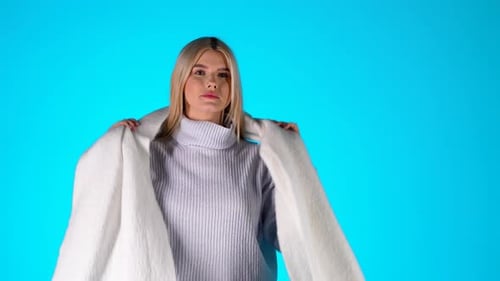 Portrait Of Young Blonde Woman Feeling Cold, Wearing Scarf Sweater and Earmuffs, Studio Shot With Bl