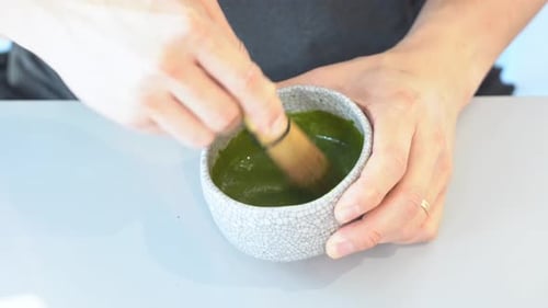 Handheld motion close up shot of a pair of hands whisking and mixing match green tea in the handmade