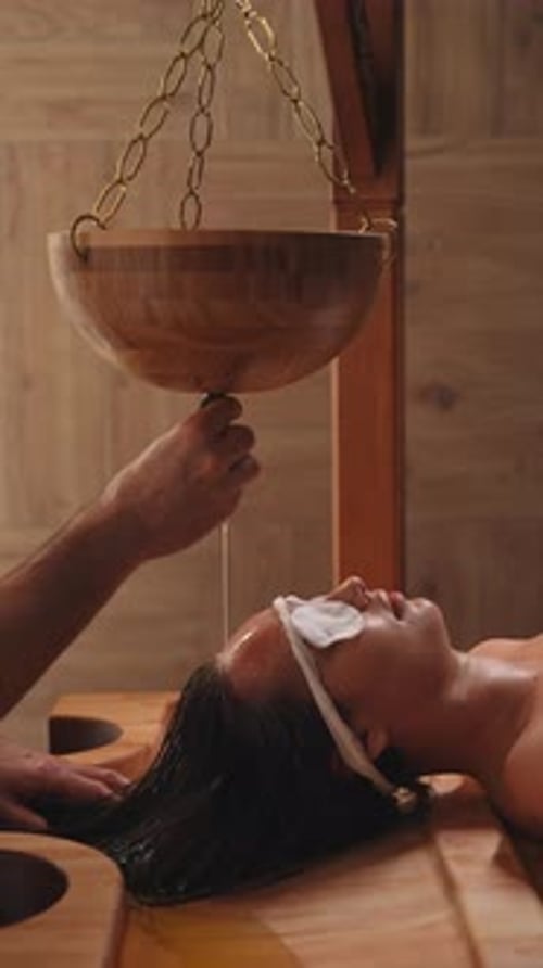 Jovem relaxada recebendo procedimento ayurvédico Shirodhara que eleva você a um estado chamado Trance