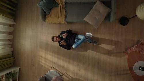 Top View of a Man Lying on the Living Room Floor with a Smartphone in His Hands The Man is Playing