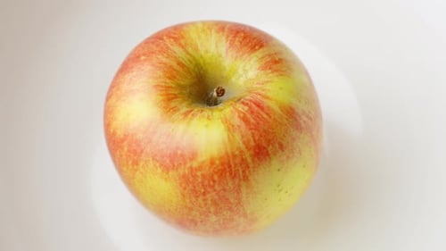 Frischer roter und gelber Apfel, der sich auf einer weißen Oberfläche in einer sauberen, hellen Nahaufnahme dreht