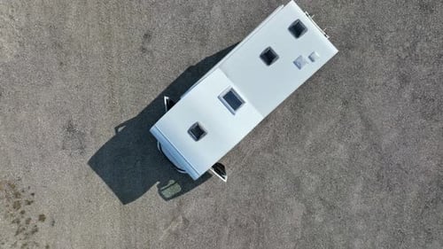 Top down drone shot of a man walking to his camper van, parked on a dirt road