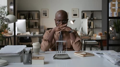 Pensive African American Sitting at Office Desk with Newtons Cradle