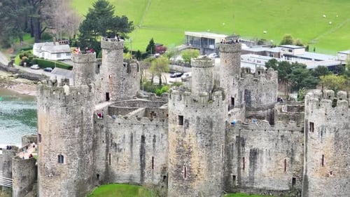 Several tourists stand on the towers of the large historic Conwy Castle to enjoy the view against th