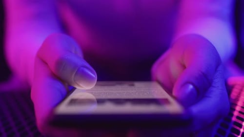 Woman scrolls through neon lit smartphone news feed in trendy vibrant colors