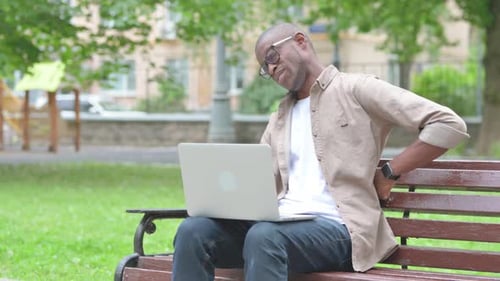 Young African Man with Back Pain While Using Laptop in Park
