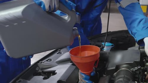 Closeup hands of mechanic man pouring motor oil in engine car in the garage.