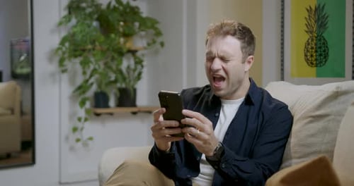 Man Laughing at Smartphone While Sitting on Sofa