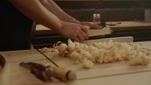 Hands planing wood with shavings on workbench in carpentry workshop