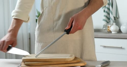 Man sharpening knife with sharpener at beige table indoors, closeup