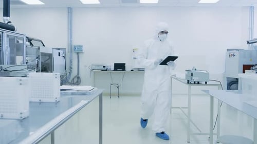 Quality Control Check: Scientist Using Digital Tablet Computer and wearing Protective Suit walks th