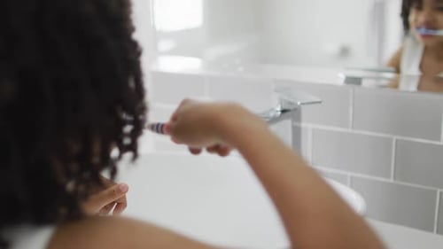 Un garçon biracial se brosse les dents dans une salle de bain lumineuse
