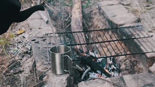 Une vieille bouilloire verse de l'eau bouillante dans une tasse touristique en fer avec du café dans la nature