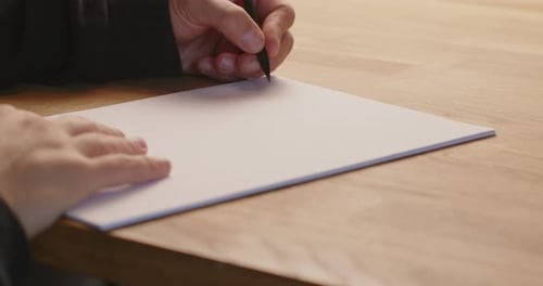 Caucasian person writing with the left hand of a peace of paper with a pencil. Static close up shot,
