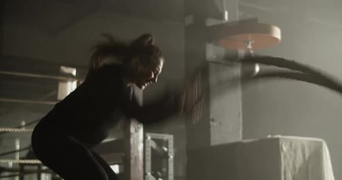 Strong Athletic Woman Training with Battle Rope in Gymnasium