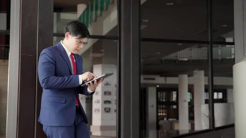 Professional young asian businessman in suit using tablet while standing in modern office.