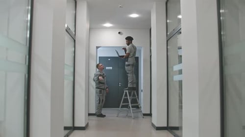 Multi Ethnic Installers in Uniform Sets Up Security Cameras in Office Corridor