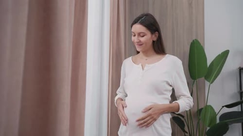 Pregnant Woman Gently Holds Her Baby Bump at Home