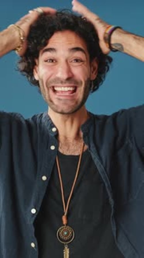 Wonder man put his hands on his head looking at camera isolated on blue background in studio