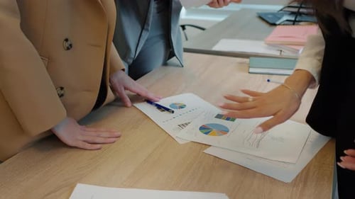Businesswomen analyzing income charts and graphs on office desk.