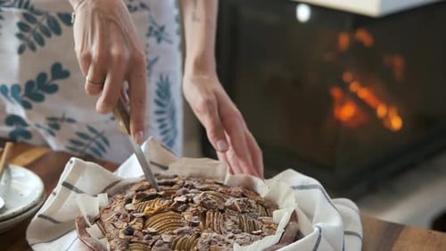 close-up woman cuts a tart knife with apples and nuts by the fireplace