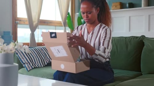 Woman Opens Box, Looks Disappointed on Couch