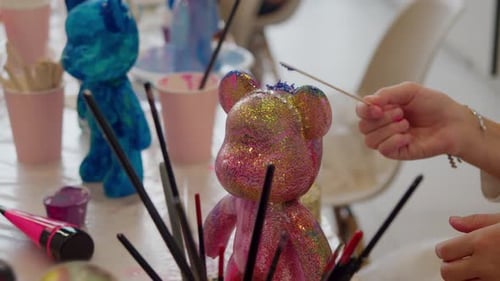 Eine rosafarbene Teddybärfigur mit einer Tiara aus künstlichen Edelsteinen wird mit einem speziellen Zauberstab blau bemalt