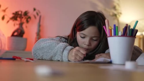Das Kind konzentriert sich aufs Zeichnen mit dem Malstift, künstlerische Kreativität mit einem Eimer voller Stifte in der Nähe
